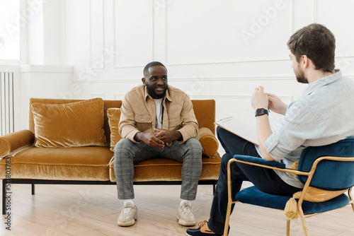 The therapist takes notes while talking to a depressed male patient and talks to an African American patient. Desperate black man suffering from nervous breakdown or depression having a session with a