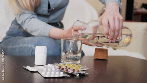 A young woman pours water into a glass, takes out a pill and takes the medicine