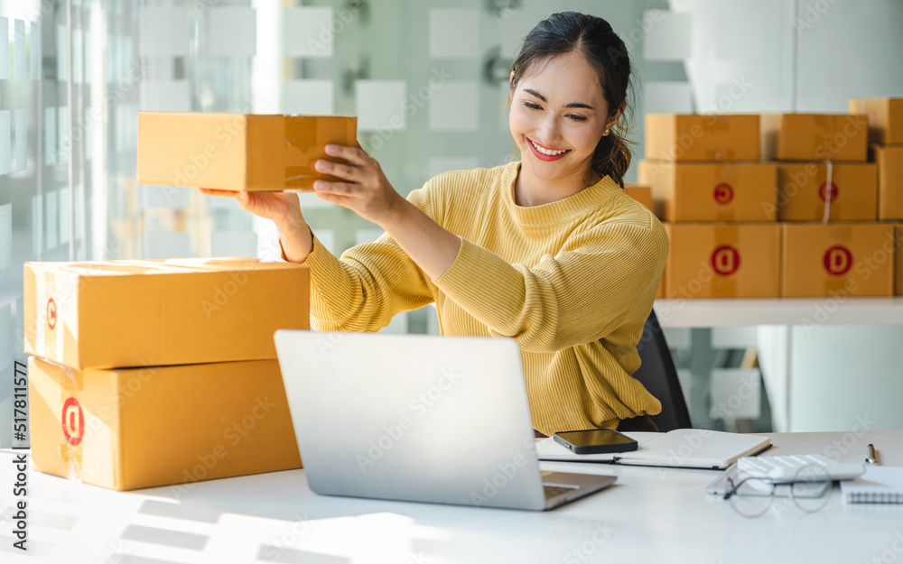 Startup small business entrepreneur or freelance Asian woman using a laptop with box, Young success Asian woman with her hand lift up, online marketing packaging box and delivery, SME concept. Startup small business entrepreneur or freelance Asian woman using a laptop with box, Young success Asian woman with her hand lift up, online marketing packaging box and delivery, SME concept.