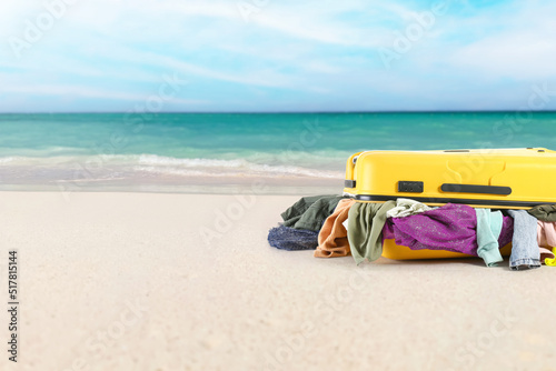 Suitcase with heap of clothes on sea beach. Travel concept