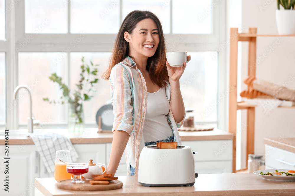 Beautiful young Asian woman with coffee and tasty toasts in kitchen Beautiful young Asian woman with coffee and tasty toasts in kitchen