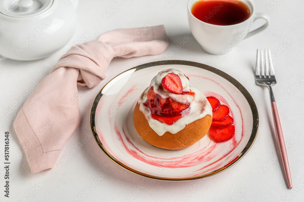 Plate with strawberry cinnamon roll and cup of tea on white background