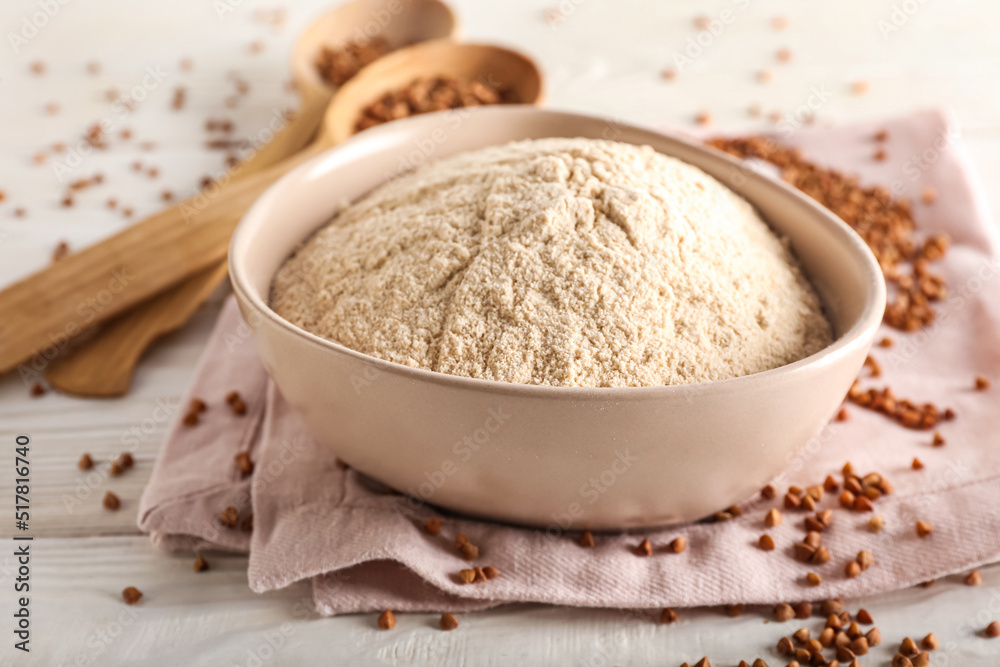 Bowl of flour with buckwheat grains and napkin on white wooden background Bowl of flour with buckwheat grains and napkin on white wooden background