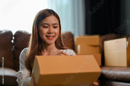 Cheerful young asian female writing a customer's address on a cardboard box