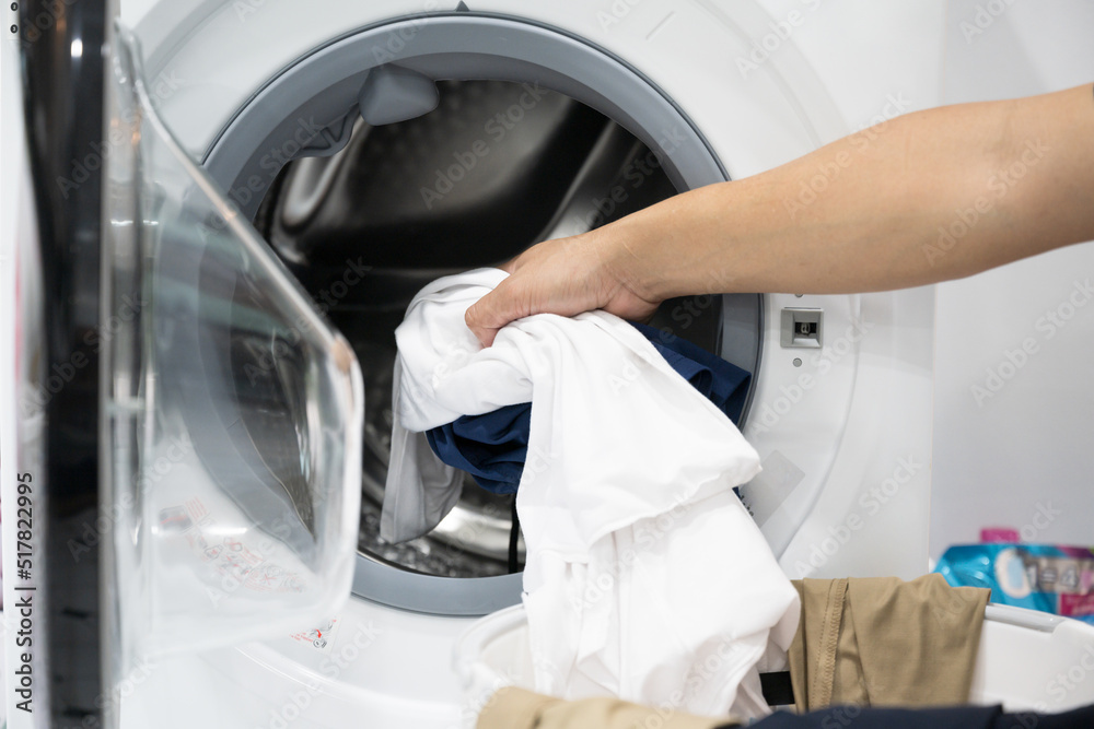 Close up hand preparing clothes in laundry room with washing machine.Housewife doing laundry at home.