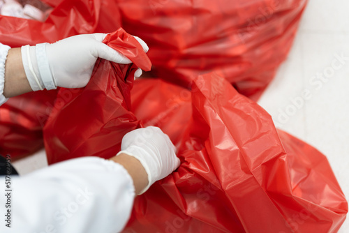 Scientist wearing white gloves and red bag with bioharzard sign.A woman worker hand holding red garbage bag.Maid and infection waste bin at the indoor public building.Infectious control.