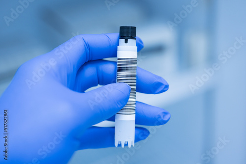Close up scientist hand wearing blue gloves and holding storage reagent container for laboratory analysis.Scientist hand holding reagent tube during prepare specimen for auto machine analysis.