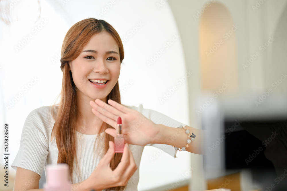 Gorgeous Asian female beauty blogger recording a beauty video, showing a lipstick to a camera