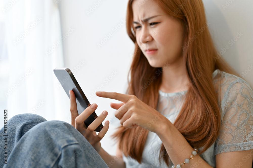 Frustrated young Asian woman using smartphone, having a problem on her phone Frustrated young Asian woman using smartphone, having a problem on her phone