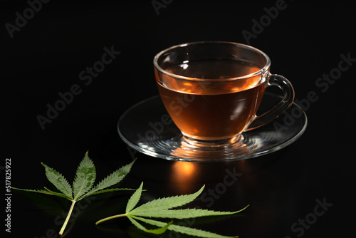 Cup with cannabis tea and marijuana leaf on black background, copy space.Herb tea for good health.