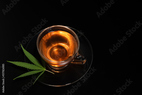 Cup with cannabis tea and marijuana leaf on black background, copy space.Herb tea for good health.