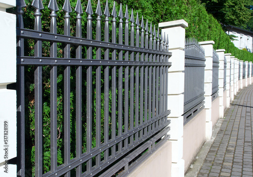 Metal fence with white posts and a green hedge.