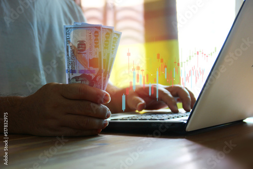 man holding dollar in hand while using laptop ckecking information current exchange on day photo