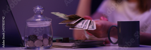 Broken young woman counting cash money, glass container with coins on desk photo