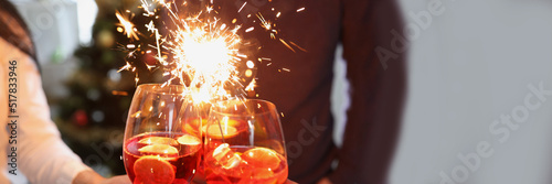 Fototapeta People raise fire sparklers and glass filled with champagne and celebrate winter