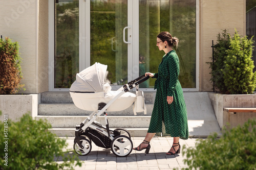 Canvas Print Young mother in a green dress on a walk with a baby in a stroller