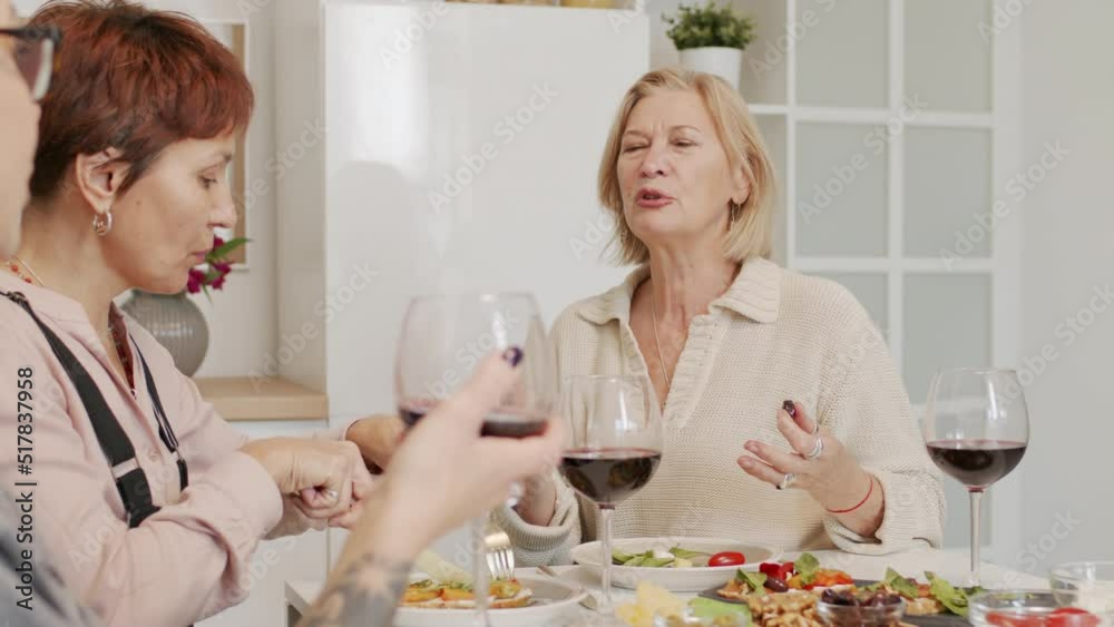 Three adult women drinking red wine and chatting while having dinner together at home Three adult women drinking red wine and chatting while having dinner together at home