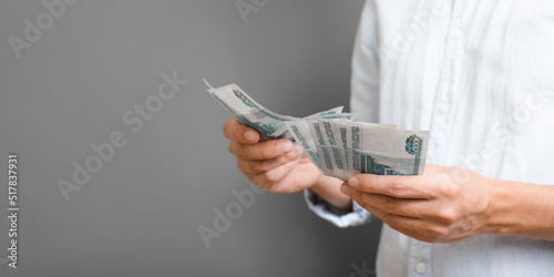 Unrecognizable person holding one thousand ruble banknotes standing on gray background, copy space. Close-up of man in shirt counting money. Banner with free place for text