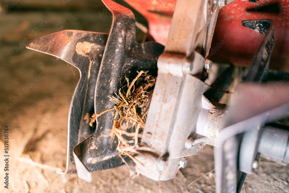 Rototiller of a walkbehind tractor with tangled dry grass closeup
