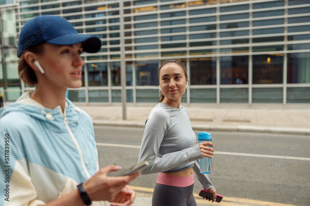 Two sportive young female friends walking city after morning running