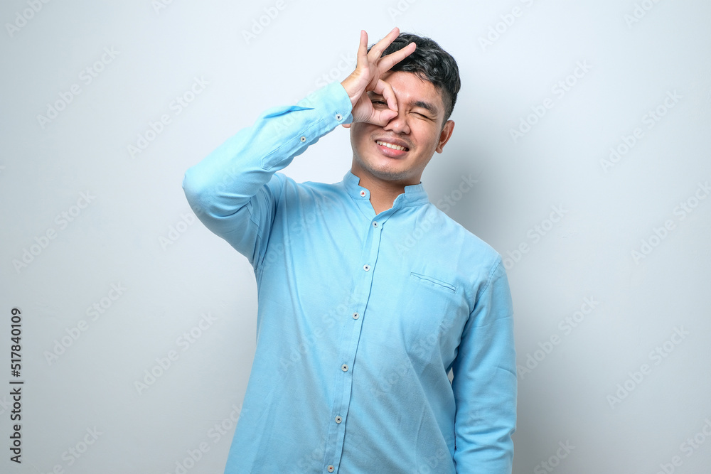 Young Asian man smiling and doing ok sign with fingers, excellent symbol
