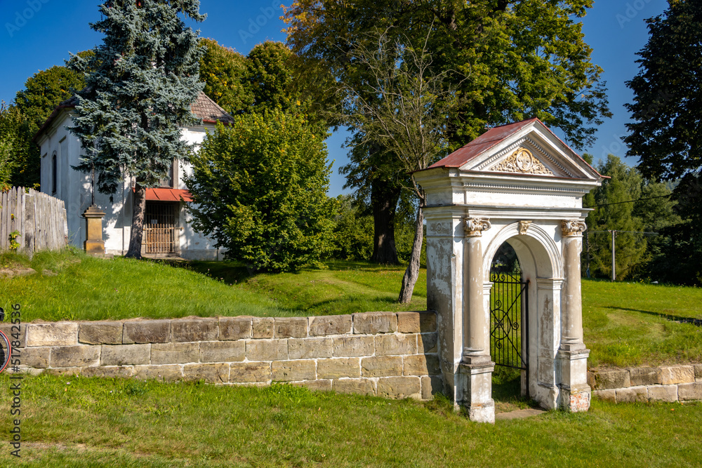 Classicist gate at the entrance to a country cemetery with a baroque chapel