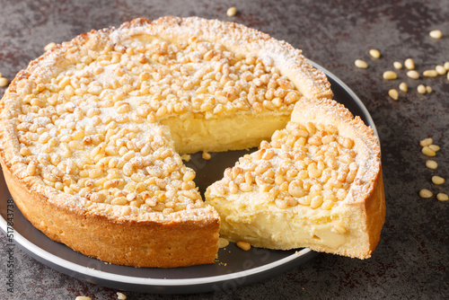 Torta della Nonna is the most delicious Italian custard tart made with sweet shortcrust pastry, custard cream and topped with pine nuts closeup in the plate on the table. Horizontal photo