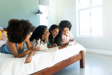 Cheerful carefree biracial young female friends using mobile phone and laughing while lying on bed