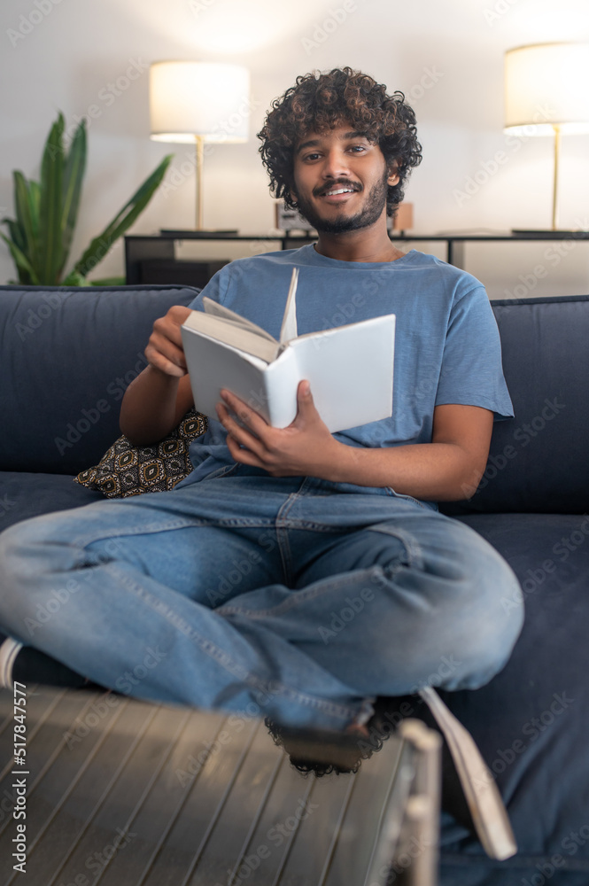 Curly-haired indian guy reading a book and looking involved Curly-haired indian guy reading a book and looking involved