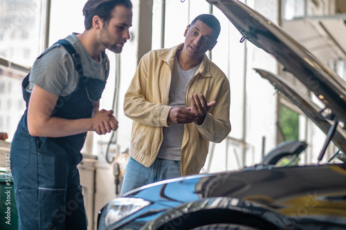 Customer looking questioningly at mechanic near hood of car