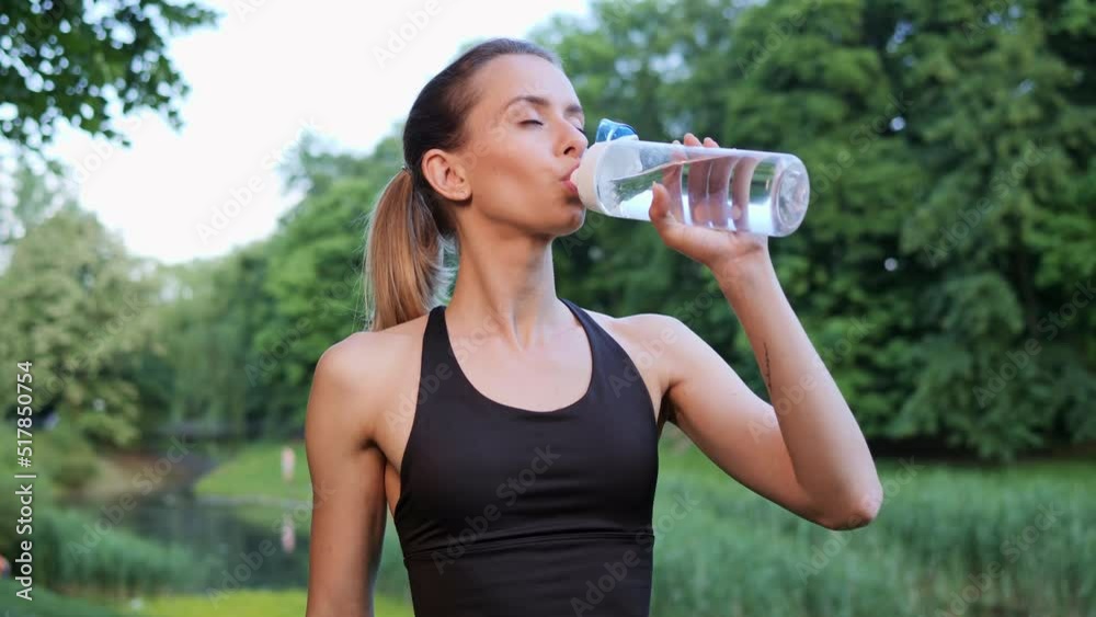 Sportswoman drinking water from sport bottle at sunset in city park Woman quenches thirst after workout green nature background. Female drink energy drink hydrating outdoor replenishing water balance. Sportswoman drinking water from sport bottle at sunset in city park Woman quenches thirst after workout green nature background. Female drink energy drink hydrating outdoor replenishing water balance.