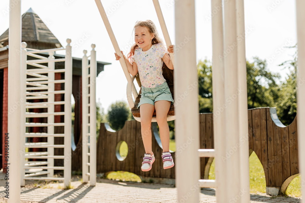 A charming girl is having fun on a swing on a summer day. Childhood, recreation, summer time A charming girl is having fun on a swing on a summer day. Childhood, recreation, summer time