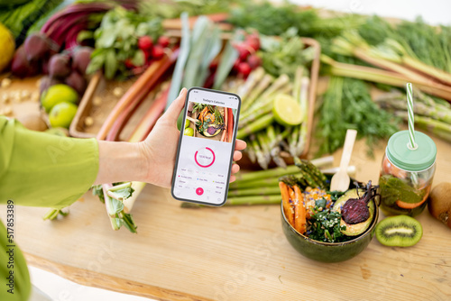 Holding smart phone with running mobile application for track calories consumed on background of healthy food ingredients. Concept of modern technology in proper nutrition photo