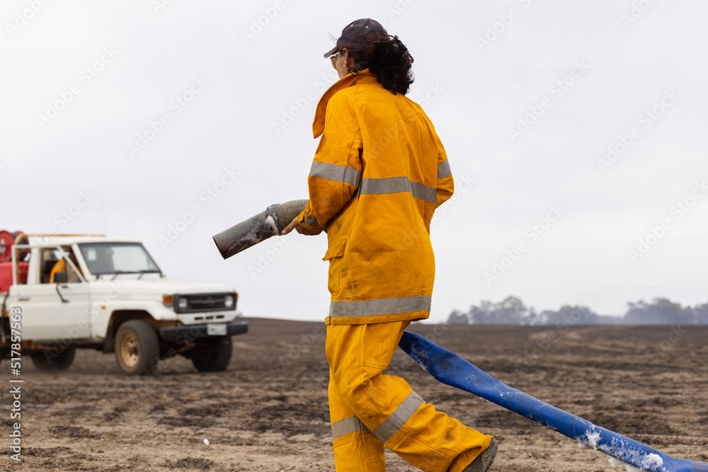Woman firefighter walking along burnt paddock holding hose