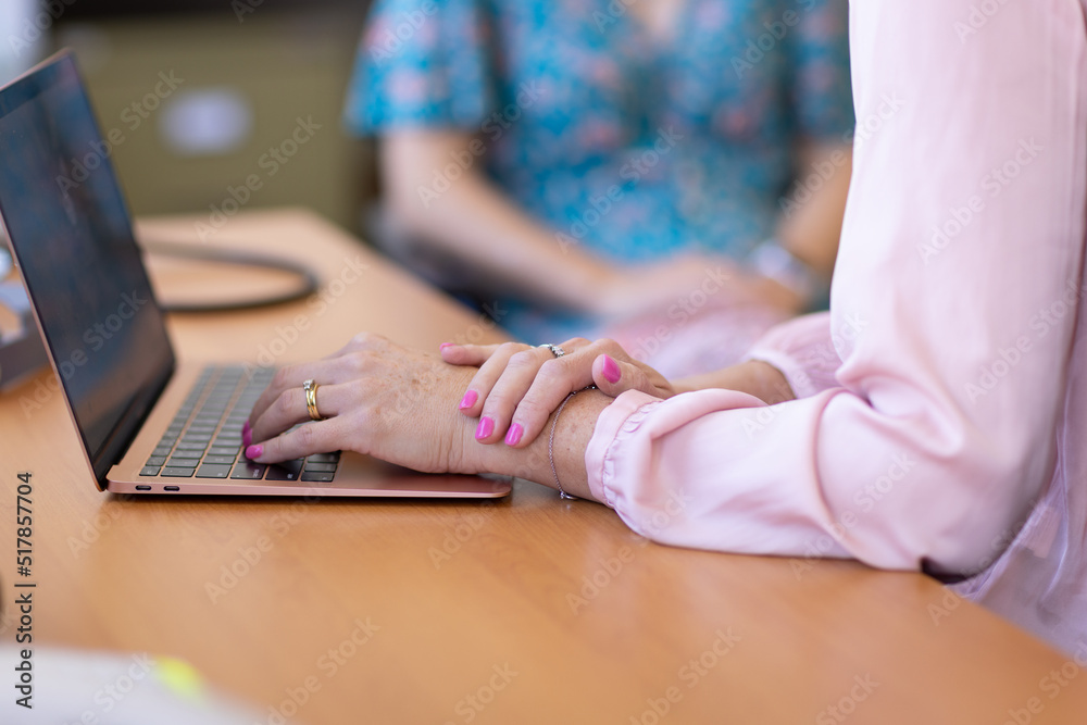 hands of professional woman with fingers on keyboard and second figure blurred in background