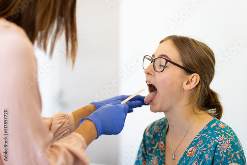 young woman in doctors surgery with doctor checking throat