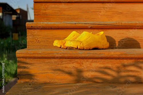 Yellow rubber muddy work shoes on old orange stairs on summer backyard at sunset, village and countryside authentic mood, low angle