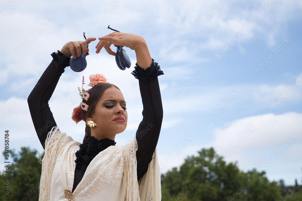 Portrait of young teenage girl in black dance dress, white shawl and pink carnations in her hair, dancing flamenco with castanets in her hands. Concept of flamenco, dance, art, typical Spanish dance. - obrazy, fototapety, plakaty 