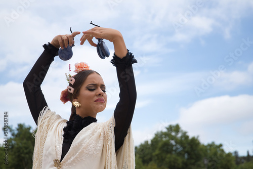 Portrait of young teenage girl in black dance dress, white shawl and pink carnations in her hair, dancing flamenco with castanets in her hands. Concept of flamenco, dance, art, typical Spanish dance. photo