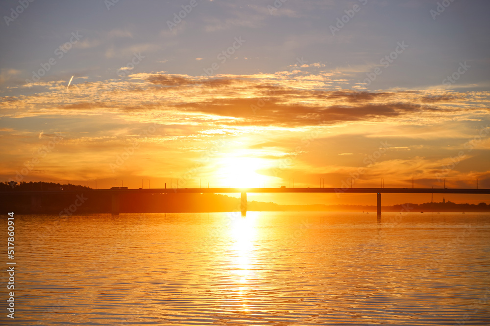 Beautiful bright orange sunset over the surface of the river and the bridge. Summer nature landscape
