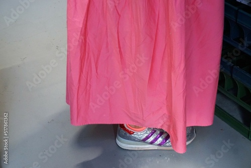 Frau mit pinkem langem Kleid und grau-lila Turnschuhen auf grauem Laminatboden 