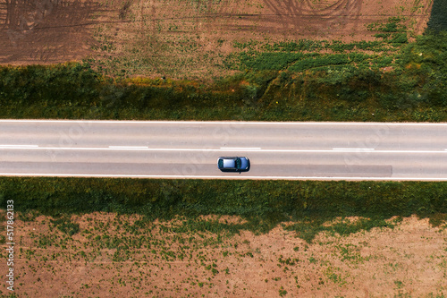 Aerial shot of passenger car driving along asphalt road through countryside landscape with no trees and shade on hot sunny summer afternoon