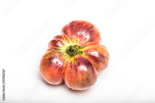 Tiger tomato on a cutting board with basil leaves on wooden background. Copy space. Fresh tomato wased for cooking. Tomato with droplets of water.