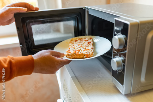 Uncooked frozen small pizza placed into the microwave.junk food,fast food concept.Side view.Selective focus.