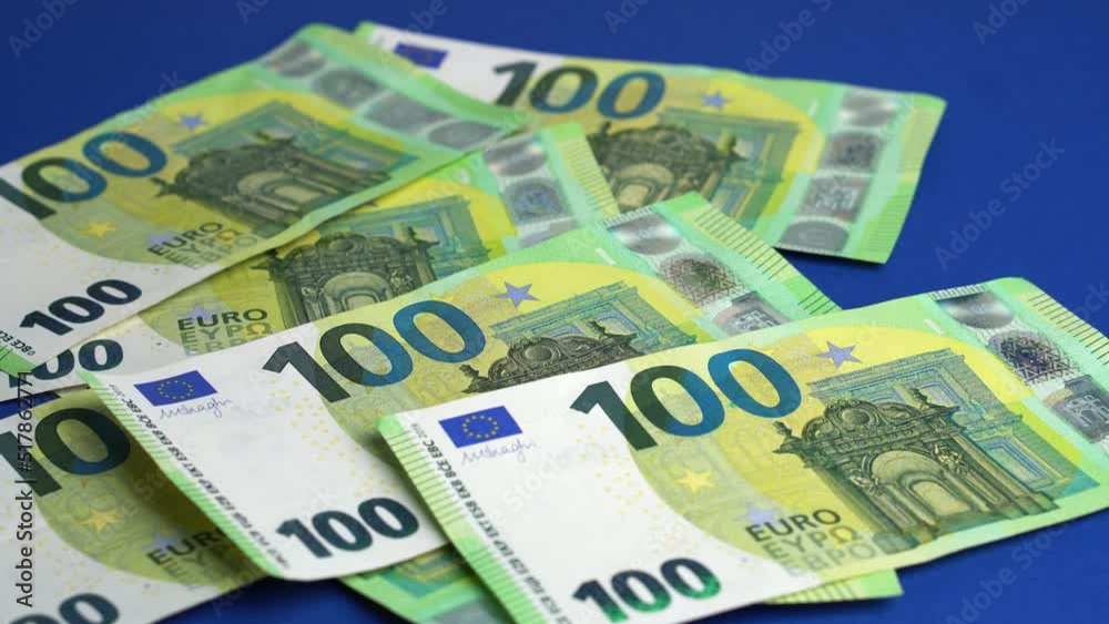 Money falling on table. Dropping lot of one hundred Euro paper banknotes on blue paper background Money falling on table. Dropping lot of one hundred Euro paper banknotes on blue paper background