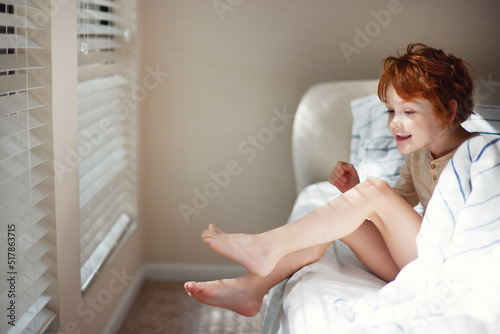 happy redhead boy is waking up in the morning in bright bedroom sunlited with morning beams through the windows blinds photo