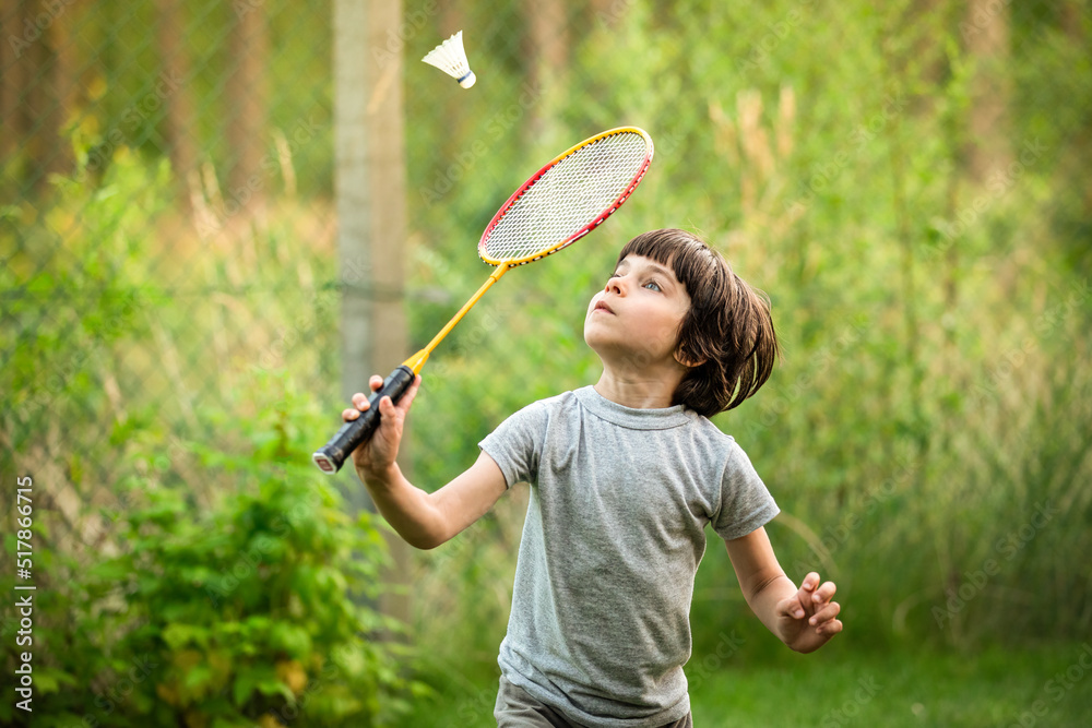 Portrait of little adorable boy playing badminton in yard outdoors in summer