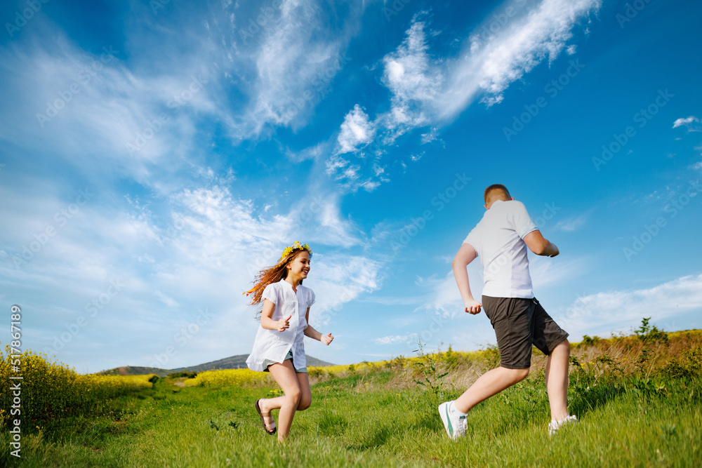 Teenagers: brother and sister are running and enjoying weather, in meadow against cloudy sky Teenagers: brother and sister are running and enjoying weather, in meadow against cloudy sky