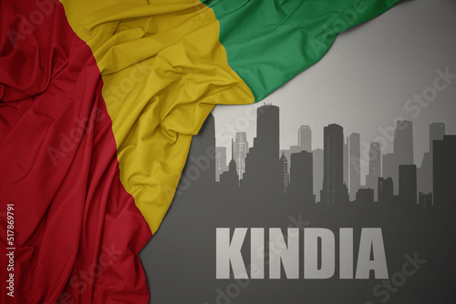 Obraz na plátne abstract silhouette of the city with text Kindia near waving colorful national flag of guinea on a gray background