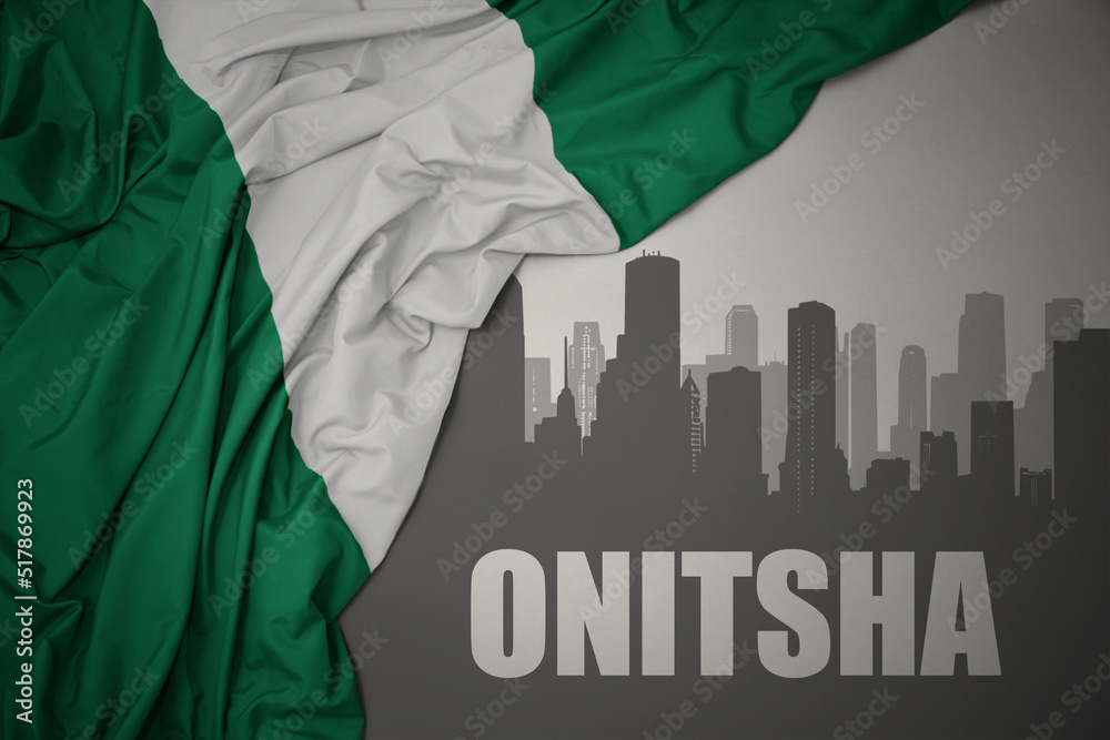 abstract silhouette of the city with text Onitsha near waving colorful national flag of nigeria on a gray background.